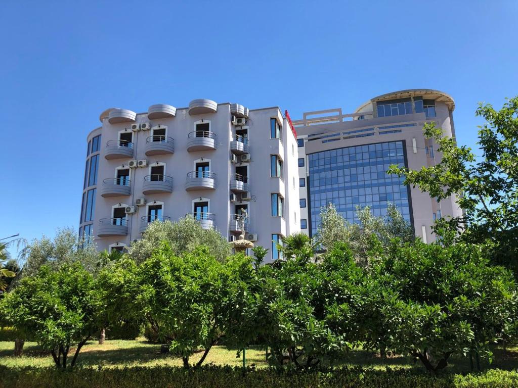 un edificio bianco con alberi di fronte di Hotel Silvio a Fier