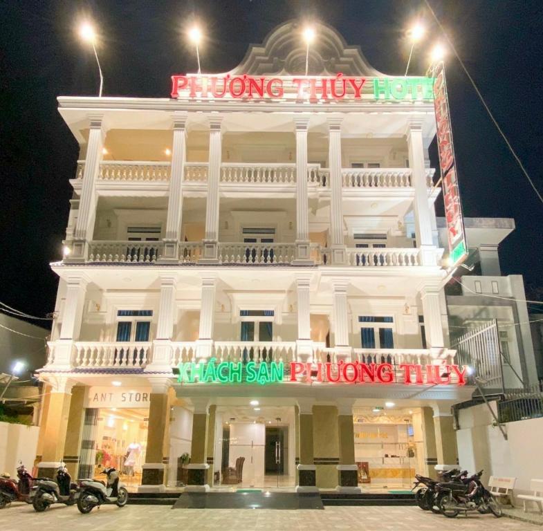 un grand bâtiment blanc la nuit avec des motos garées devant dans l'établissement Phuong Thuy Hotel, à Cần Thơ