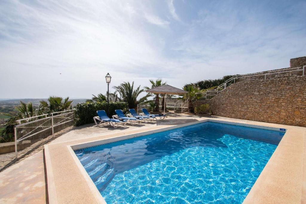 a swimming pool with chairs and a house at Ghar Ilma IV Holiday Home in Santa Luċija