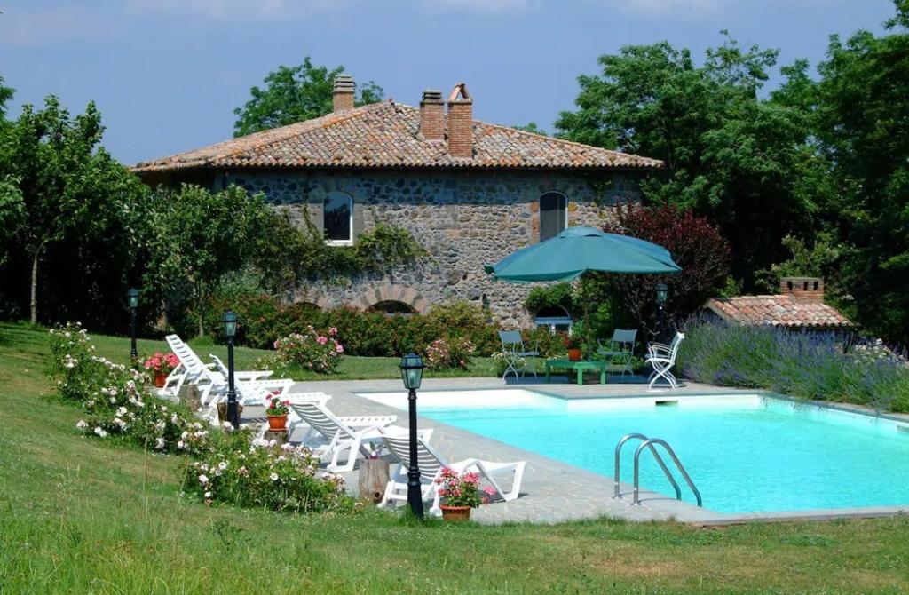 a pool in front of a house with chairs and an umbrella at Collina Blu in Bolsena