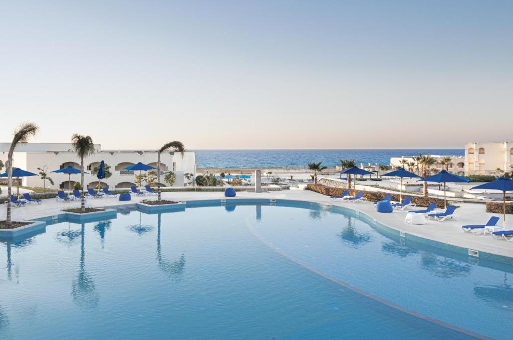 a large swimming pool with chairs and umbrellas and the ocean at Cleopatra Luxury Resort Sidi Heneish - North Coast in Marsa Matruh
