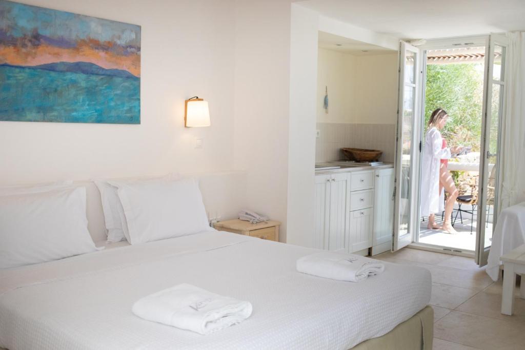 a white bedroom with a bed and a woman standing outside at Kavos Hotel Naxos in Agios Prokopios