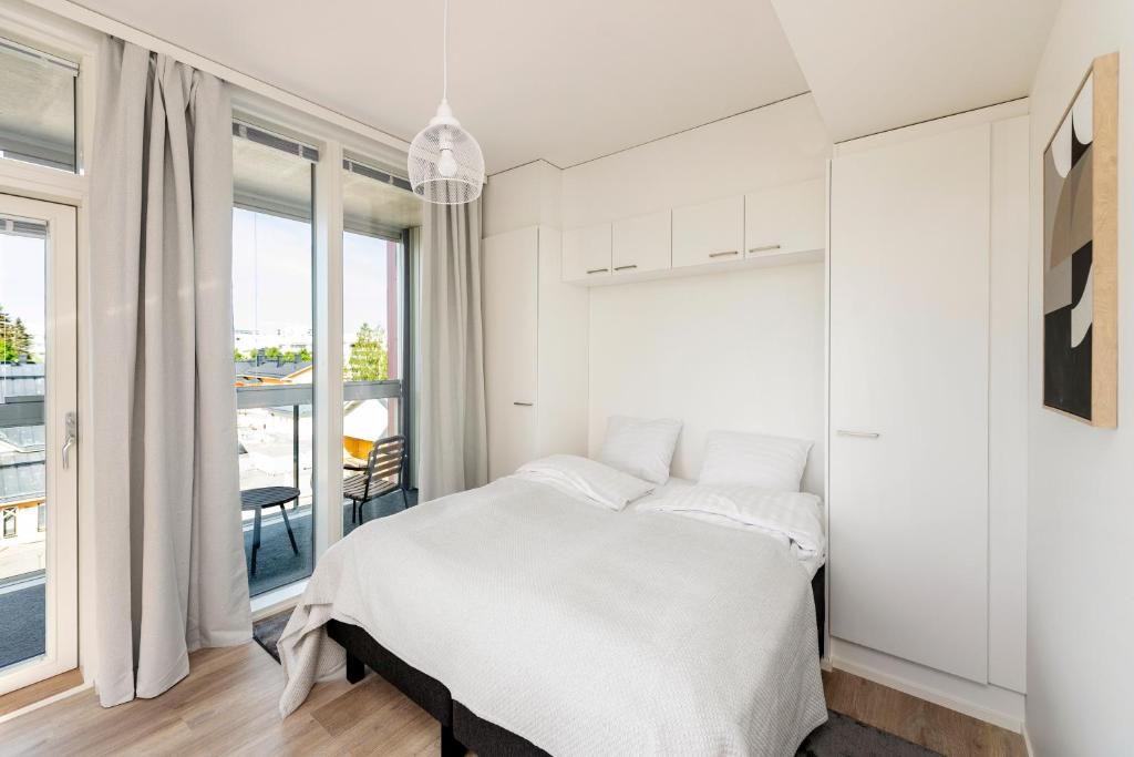 a white bedroom with a bed and a balcony at Kotimaailma Apartments Loimu III in Oulu