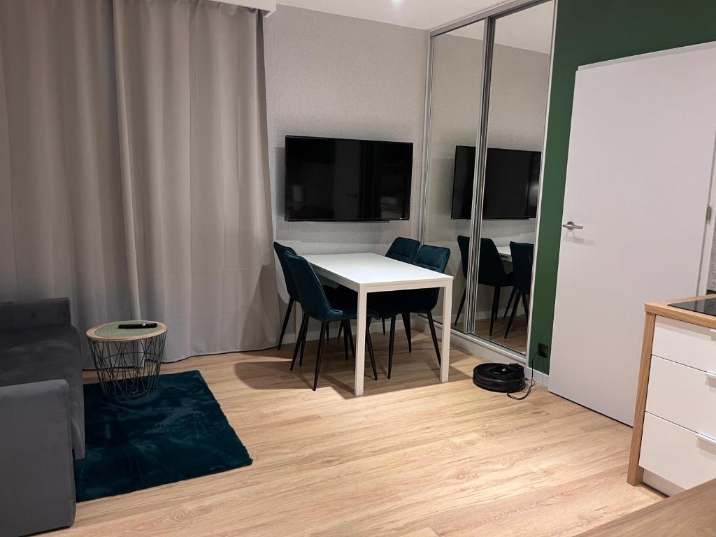 Compact living area with white dining table, teal chairs, wall-mounted TV, mirrored wardrobe, wooden floor.
