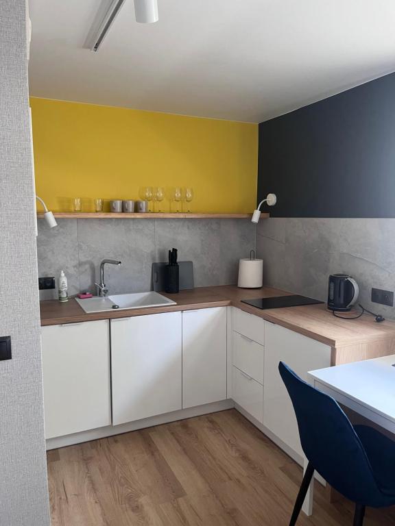 Small L-shaped kitchenette with yellow accent wall, sink, wooden countertop, black kettle, modern tiles.