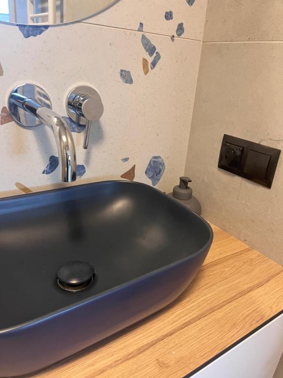 Matte navy sink on wooden vanity with terrazzo-patterned wall tiles and chrome faucet.