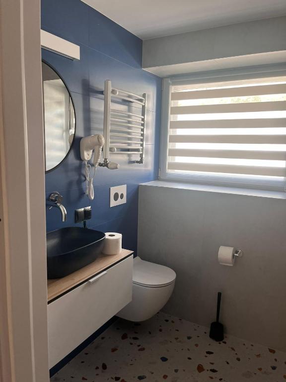 Compact bathroom with blue tiled wall, round mirror, black vessel sink and striped window blind.