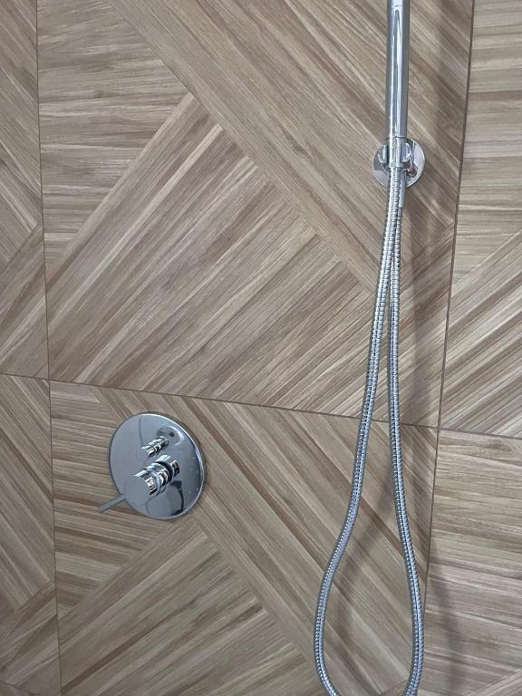 Chrome handheld shower and control knobs mounted on geometric wood-patterned bathroom tiles.