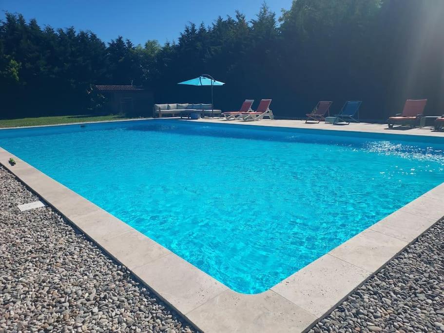 una gran piscina azul con sillas y sombrilla en Grand gite à colombage - Moulin à eau en Bournel
