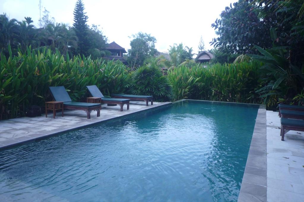 a swimming pool with benches next to a resort at Gerebig Bungalow in Ubud