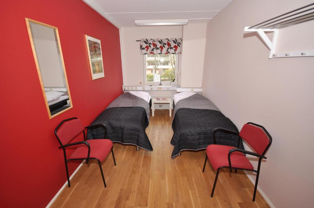 Duas camas num quarto com paredes vermelhas e cadeiras em Brandbergens Vandrarhem em Haninge