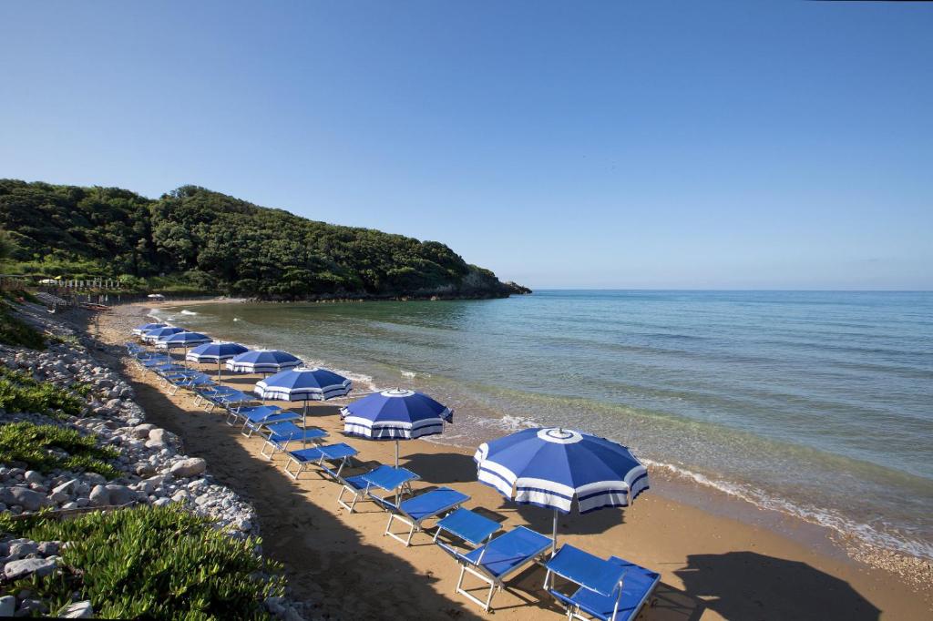 una playa con sombrillas azules y blancas y el océano en Torre San Vito Hotel Villaggio, en Gaeta