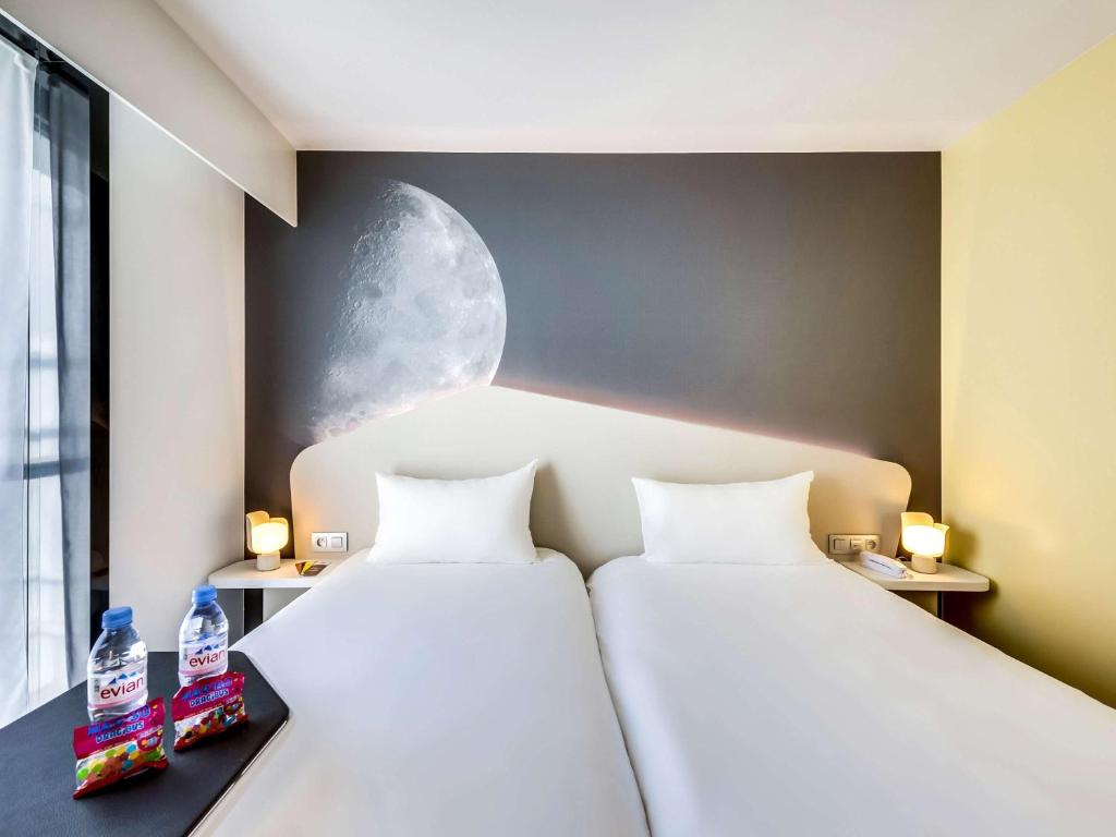 two beds in a room with two bottles of water at ibis Styles Paris Charles de Gaulle Airport in Roissy-en-France