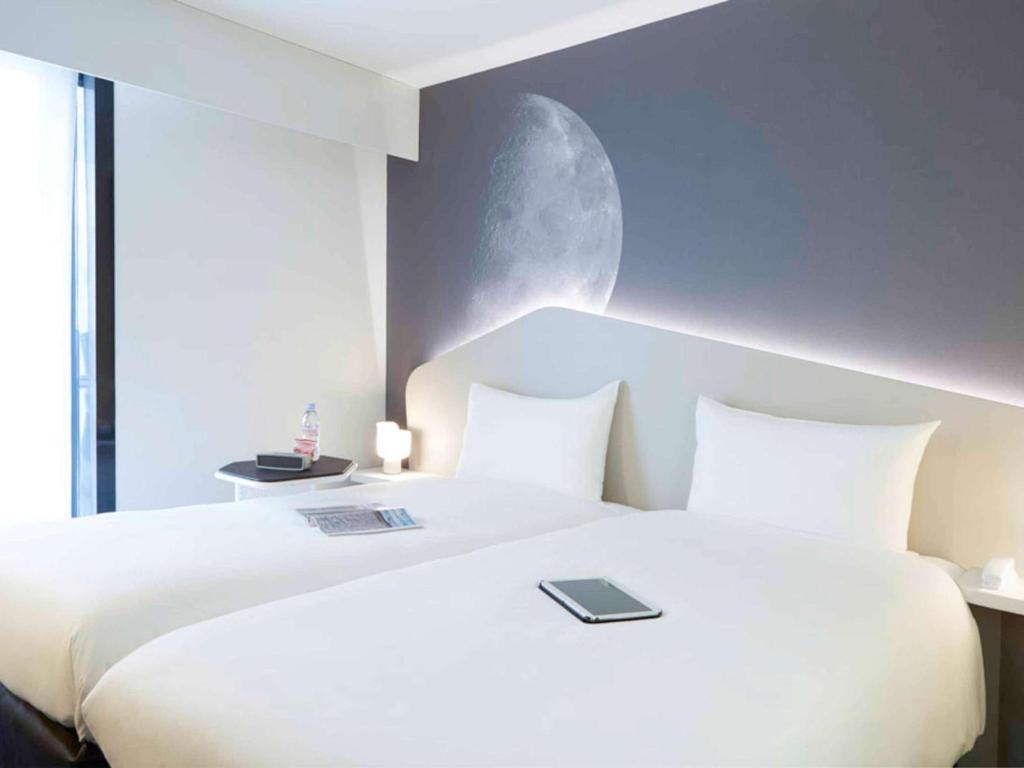 a bedroom with a large white bed with a moon on the wall at ibis Styles Paris Charles de Gaulle Airport in Roissy-en-France