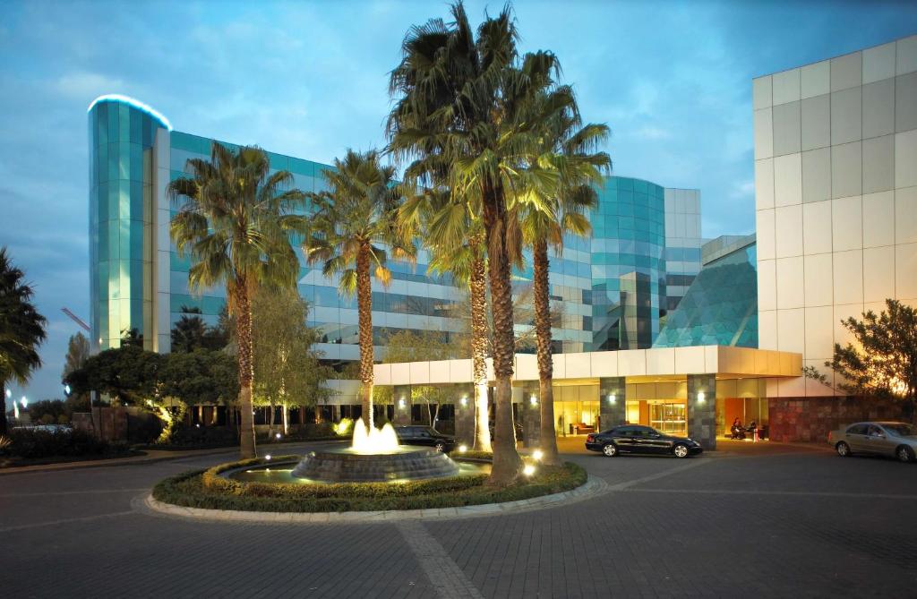 a building with palm trees in a parking lot at Southern Sun OR Tambo International Airport in Kempton Park