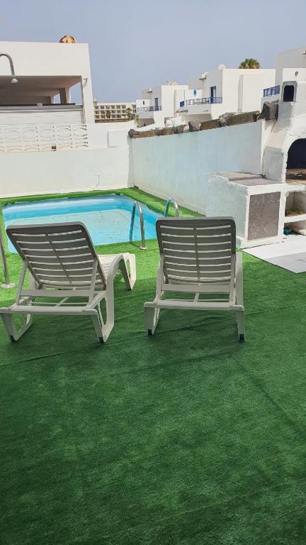 two benches sitting on the grass next to a swimming pool at Marina Lucky in Playa Blanca