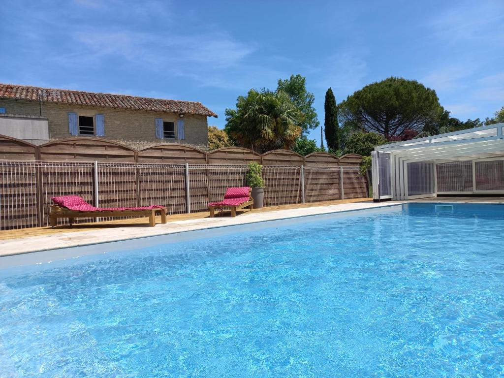 - une piscine avec 2 chaises roses à côté d'une clôture dans l'établissement Domaine de Fontsauzine - gîtes et chambre d'hôtes, à Genouillé