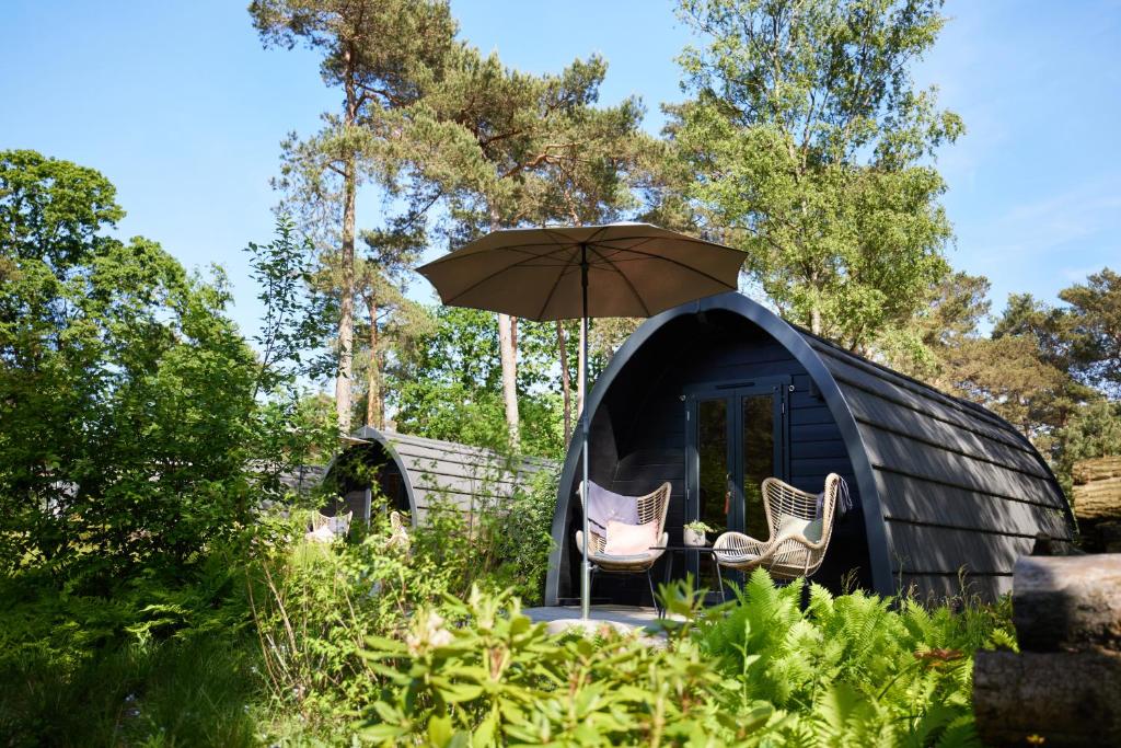 ein schwarzes Kuppelzelt mit zwei Stühlen und einem Regenschirm in der Unterkunft Kampinastaete, hippe cottages midden in natuurgebied de Kampina Oisterwijk in Oisterwijk
