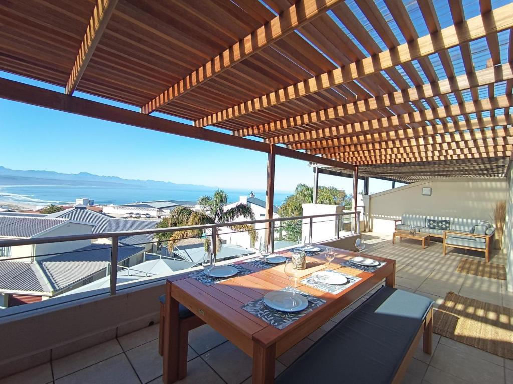 a wooden table on a balcony with a view of the ocean at Ursula's Upmarket Apartment - Panoramic Views, Large Patio - Braai, WIFI - DSTV in Plettenberg Bay