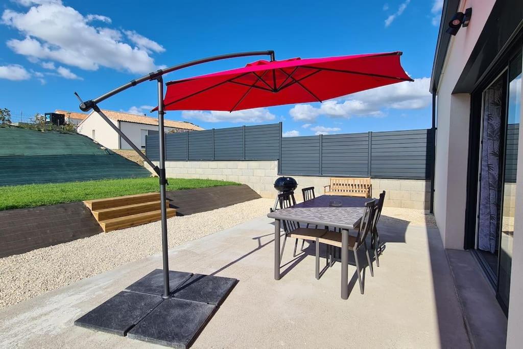 un ombrellone rosso su un patio con tavolo di Gîte la Couzinette 3km du parc Puy du Fou a Les Épesses