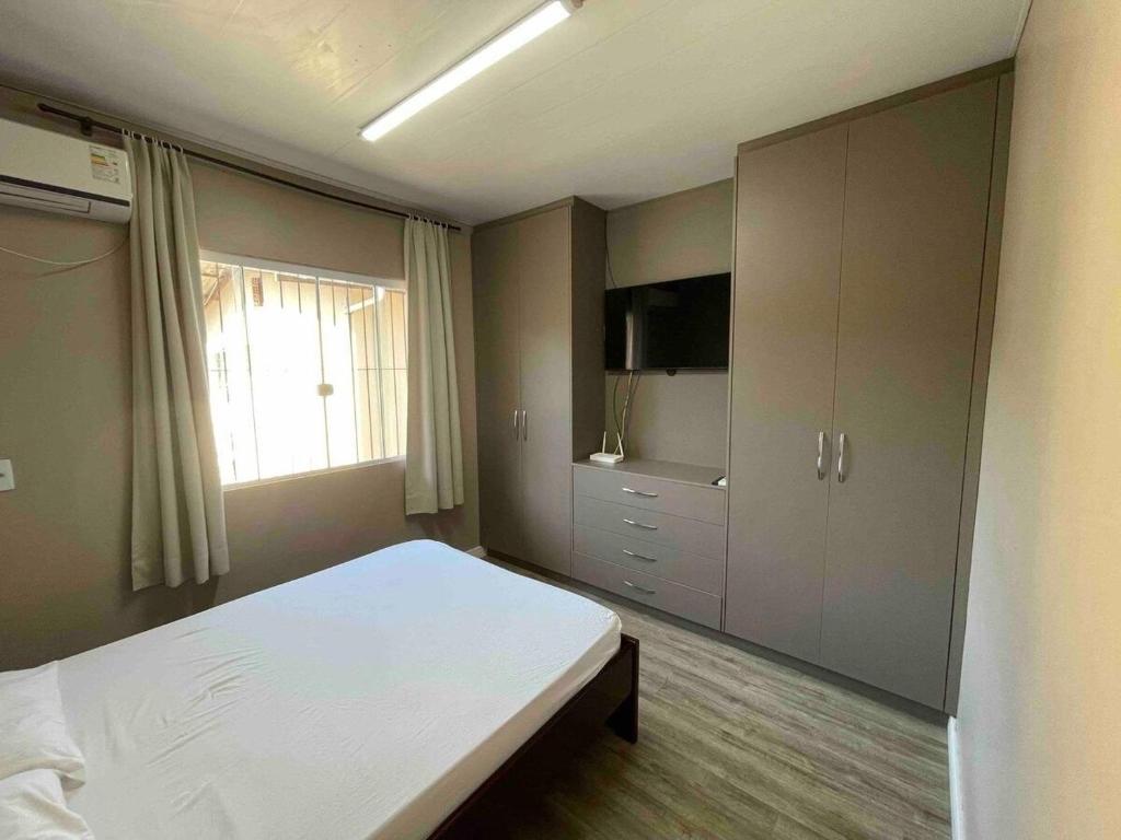 1 dormitorio con 1 cama, TV y ventana en A Jóia de Blumenau Home Office e Garagem Coberta, en Blumenau