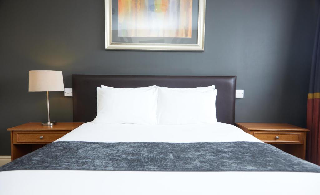 1 dormitorio con 1 cama blanca grande y 2 mesitas de noche en The Broughton Hotel by Greene King Inns, en Milton Keynes