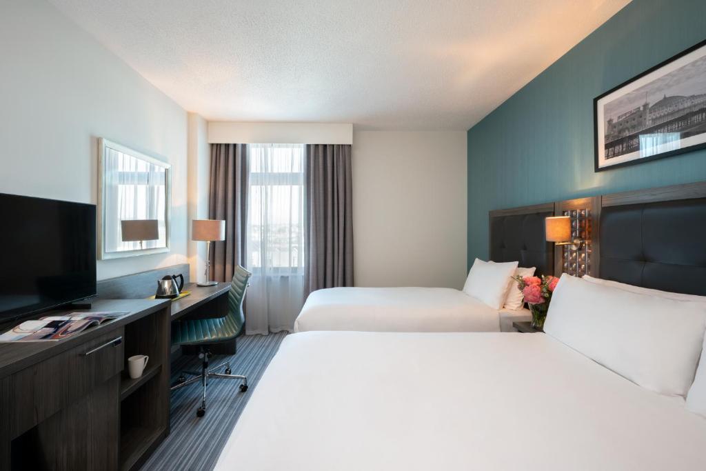 a hotel room with two beds and a desk and a television at Leonardo Hotel Brighton in Brighton & Hove