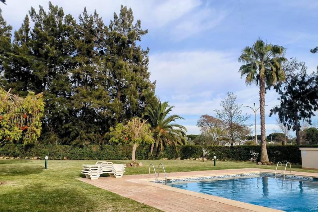 a swimming pool in a park with two white chairs and trees at Casa das Mélias in Quarteira
