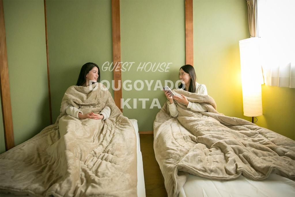 duas mulheres sentadas em camas num quarto em GUEST HOUSE DOUGOYADO KITA em Matsuyama