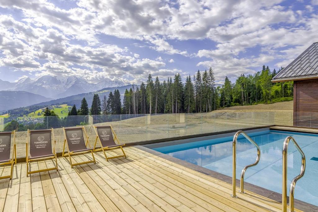 a deck with chairs and a swimming pool with mountains at La Suite Édelweiss - Welkeys in Combloux
