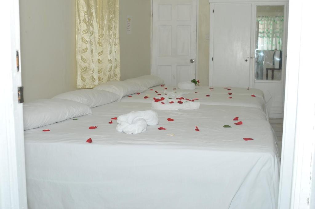 a white bed with red rose petals on it at Hilltop View Guesthouse in Castries