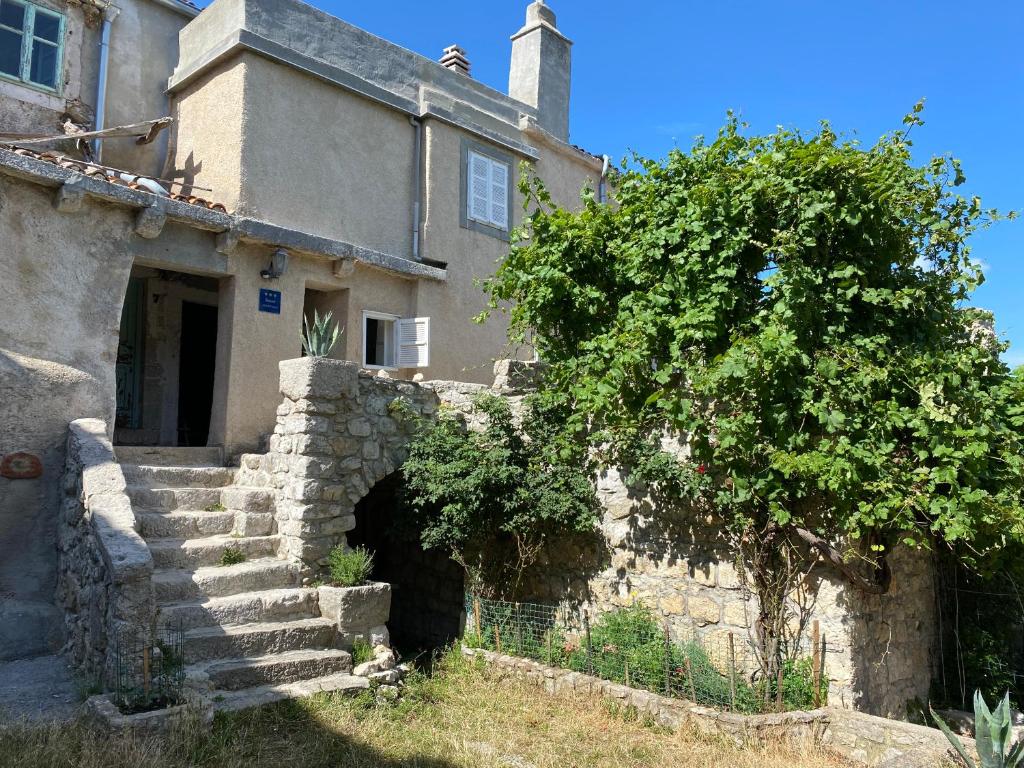 an old stone house with stairs and a tree at Apartman Nives in Lubenice