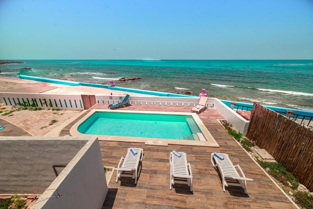 a swimming pool with chairs next to the ocean at Hotel La Trigueña in Isla Mujeres
