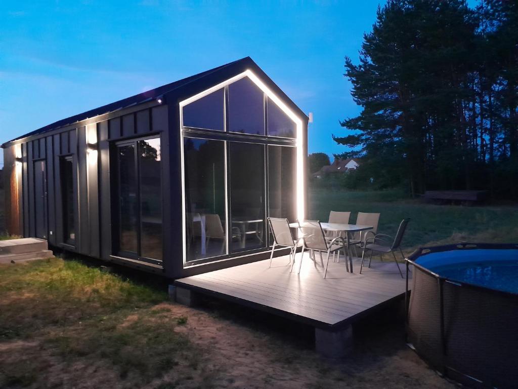 a black tiny house with a deck and a table and chairs at Domki letniskowe Jastrzębna in Sztabin