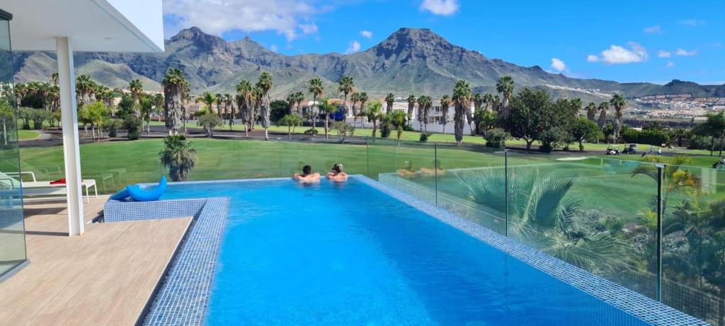 two people sitting in a swimming pool with mountains in the background at Luxury Villa Rebeka - Heated Pool and Jacuzzi in Adeje