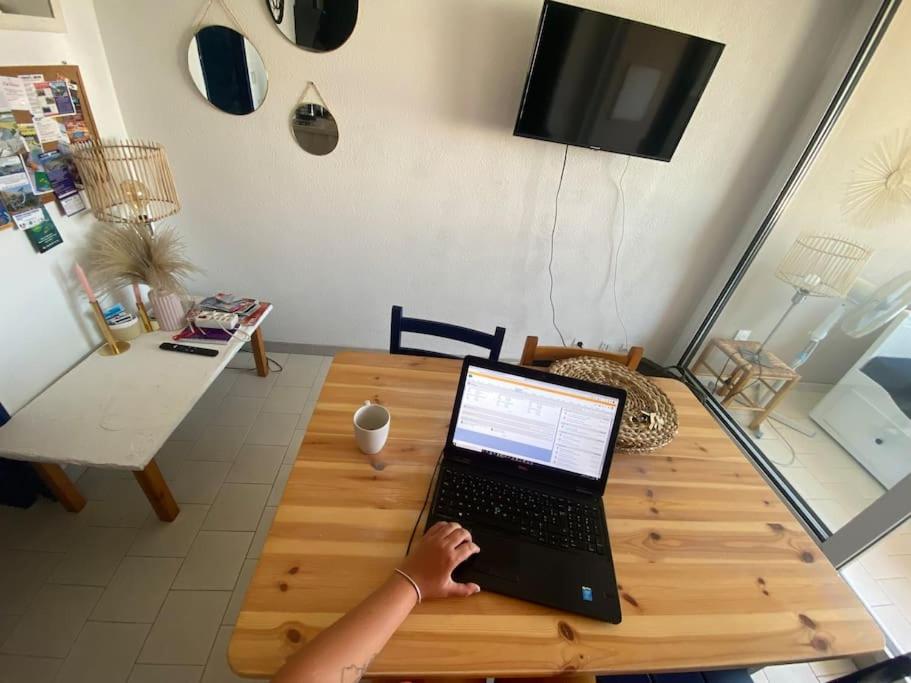 a person is using a laptop on a wooden table at Logement entier 6 pers à 500m de la plage in Sète