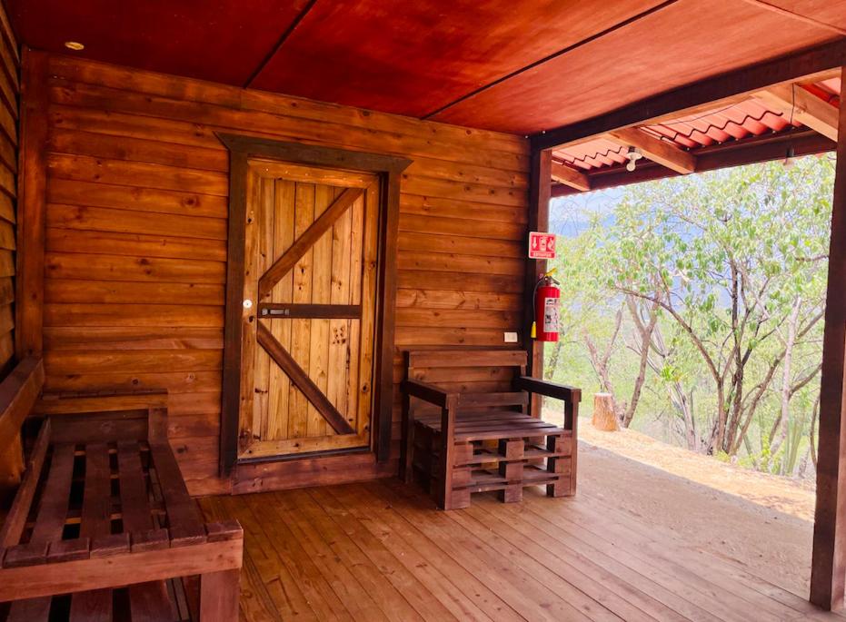 een houten hut met een deur en banken op een veranda bij Los Agaves 