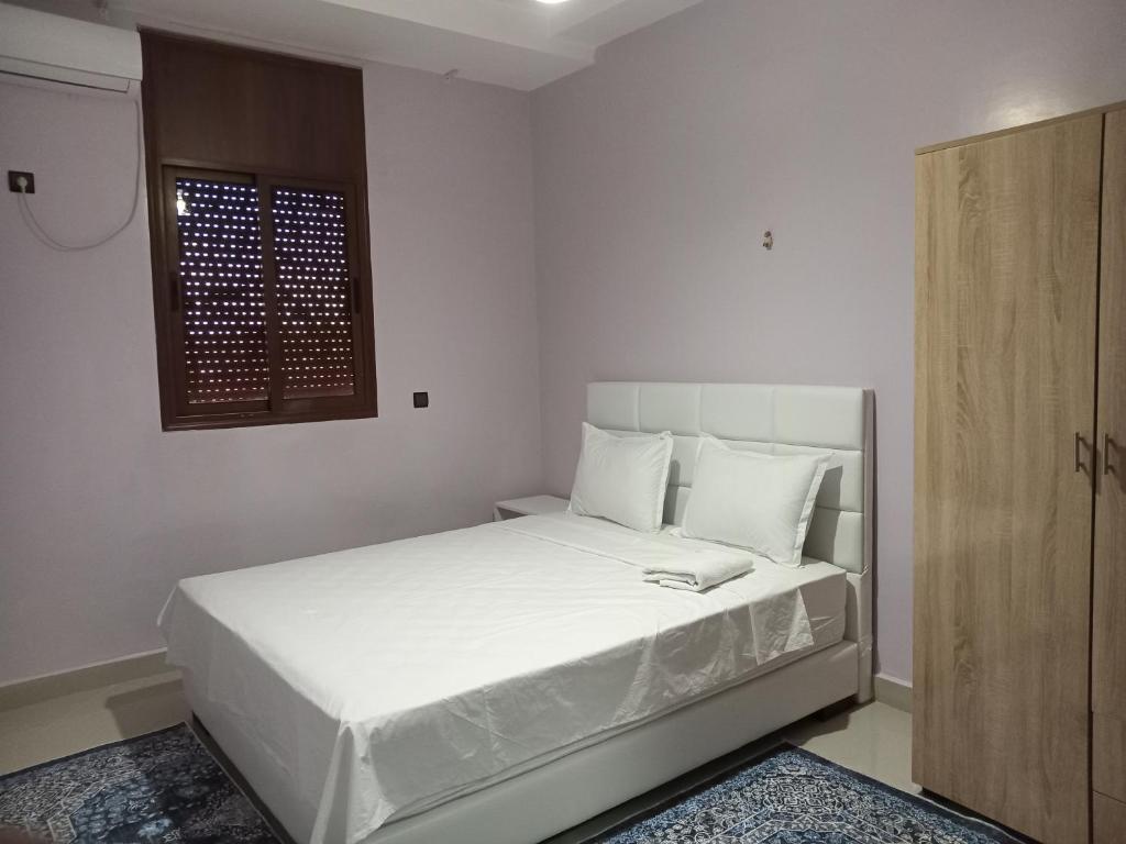 1 dormitorio con 1 cama con sábanas blancas y ventana en Résidence Jannat, en Ouarzazate