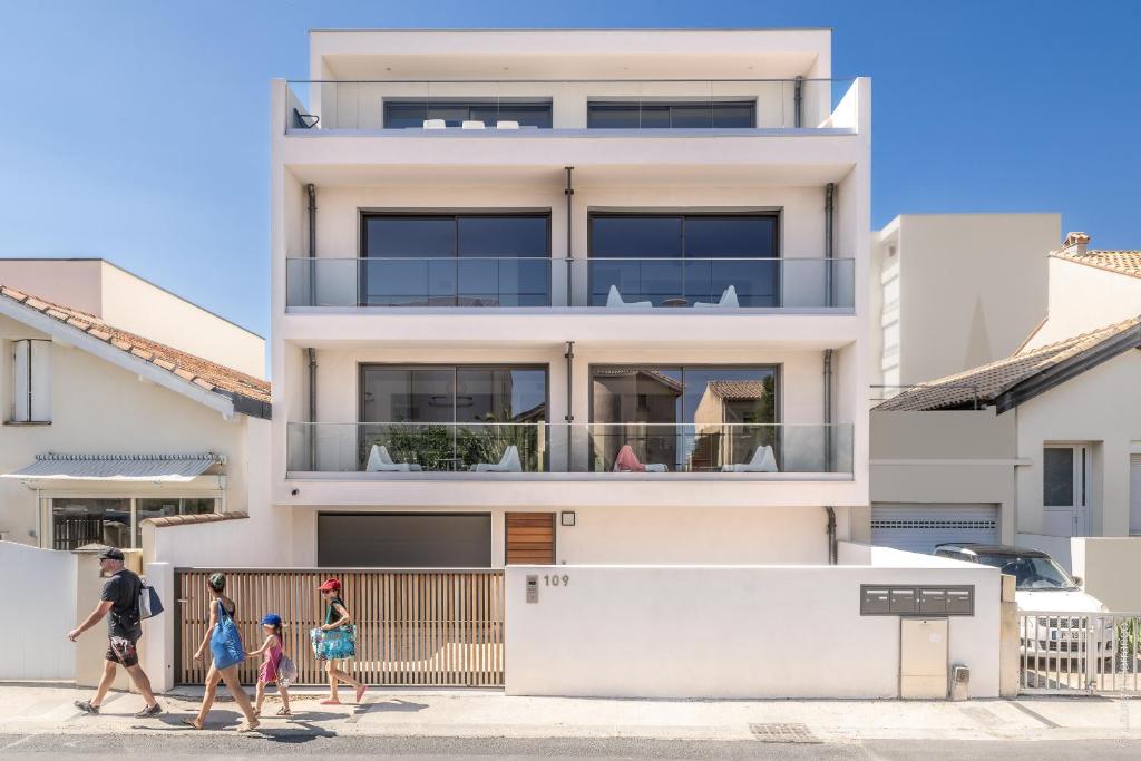 una familia camina delante de una casa en Superbe T2 neuf haut de gamme, climatisé, parking gratuit, 2eme ligne balcon, jardin en Carnon-Plage