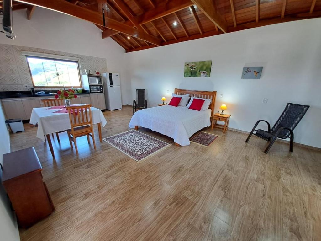a bedroom with a bed and a table and a kitchen at Chalés Conforto Mineiro in Gonçalves