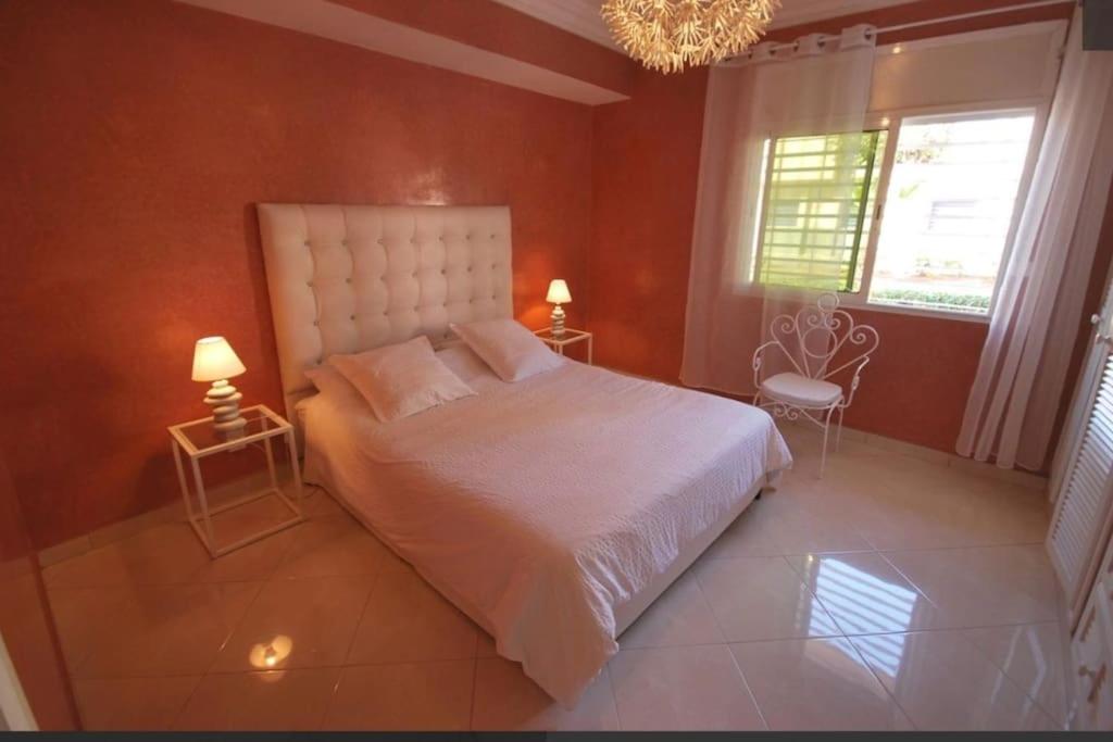 um quarto com uma cama branca, 2 candeeiros e um lustre em Logement entier avec terrasse em Agadir