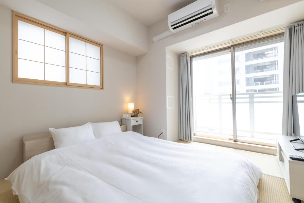 a white bedroom with a large bed and a window at Rewitビル in Osaka