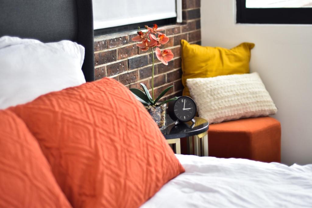 a bed with an orange pillow and a clock on a table at Moderno, cómodo y lindo departamento en Tijuana BC in Tijuana