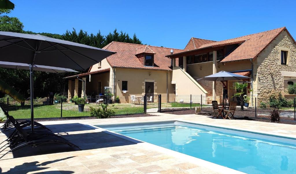 a swimming pool with an umbrella and a house at Le 4 in Montignac