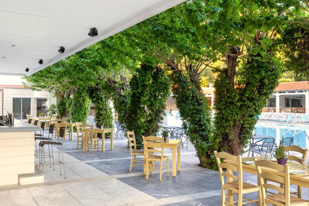 an outdoor patio with tables and chairs and trees at Sun Beach Hotel in Agia Triada