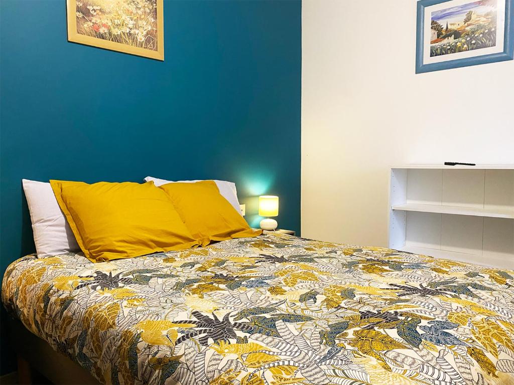 a bed with a yellow pillow and a blue wall at Auberge des Plaines - Appartements avec terrasse in Arles