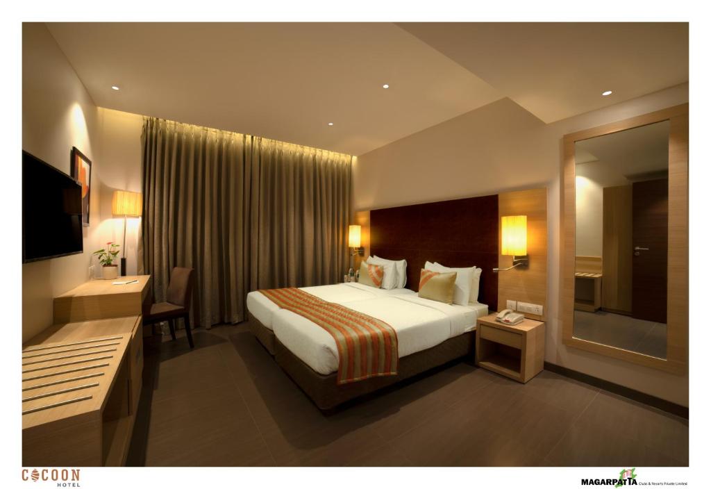 プネにあるCocoon Hotelの大きなベッドと鏡が備わるホテルルームです。