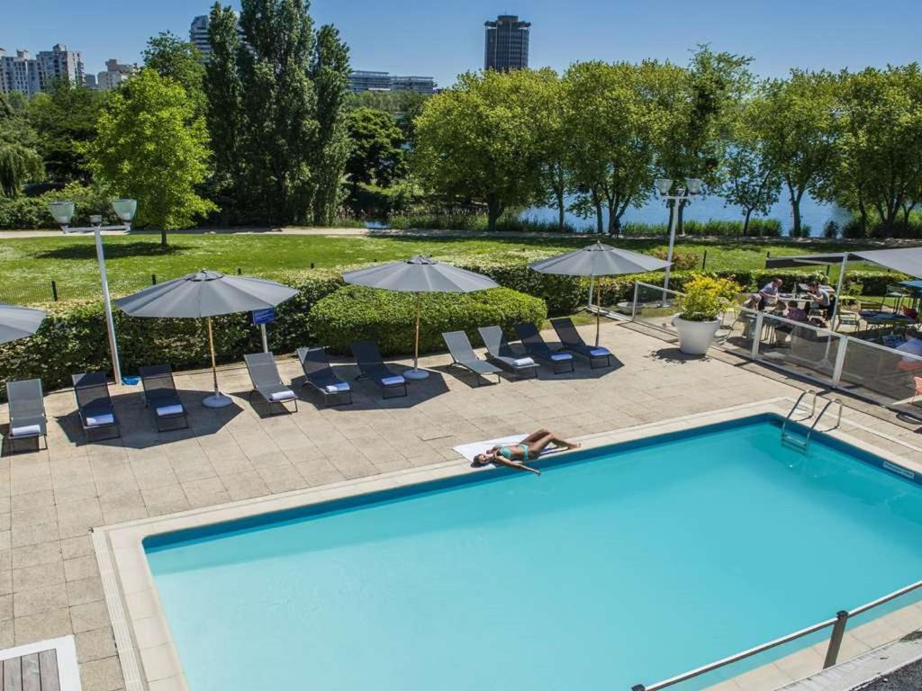 une grande piscine avec chaises et parasols dans l'établissement Novotel Paris Créteil Le Lac, à Créteil