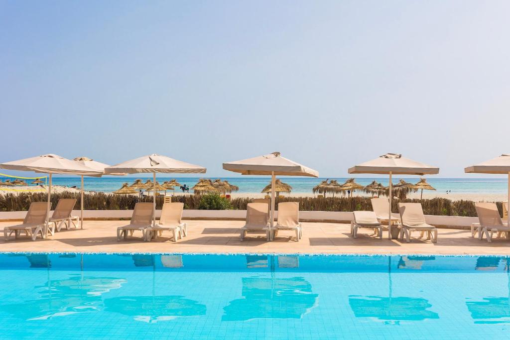 una piscina con sedie e ombrelloni accanto all'oceano di TMK Marine Beach - All Inclusive Seafront resort a Triffa
