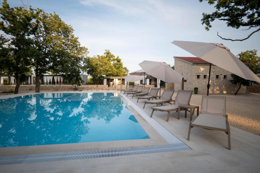 a pool with chairs and umbrellas next to a building at Dionis Zaton - Camping, Glamping, Holiday Houses & Rooms in Zaton